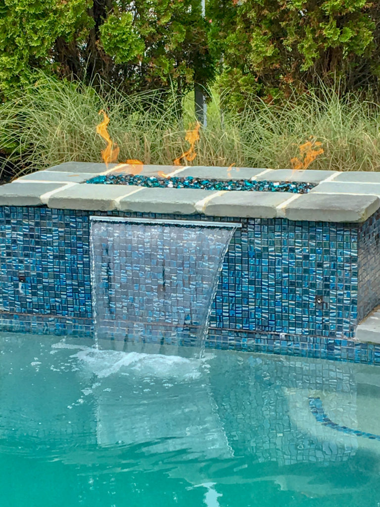 Magnarelli B - Avalon, NJ - A fire pit with a waterfall in the middle of a swimming pool surrounded by greenery