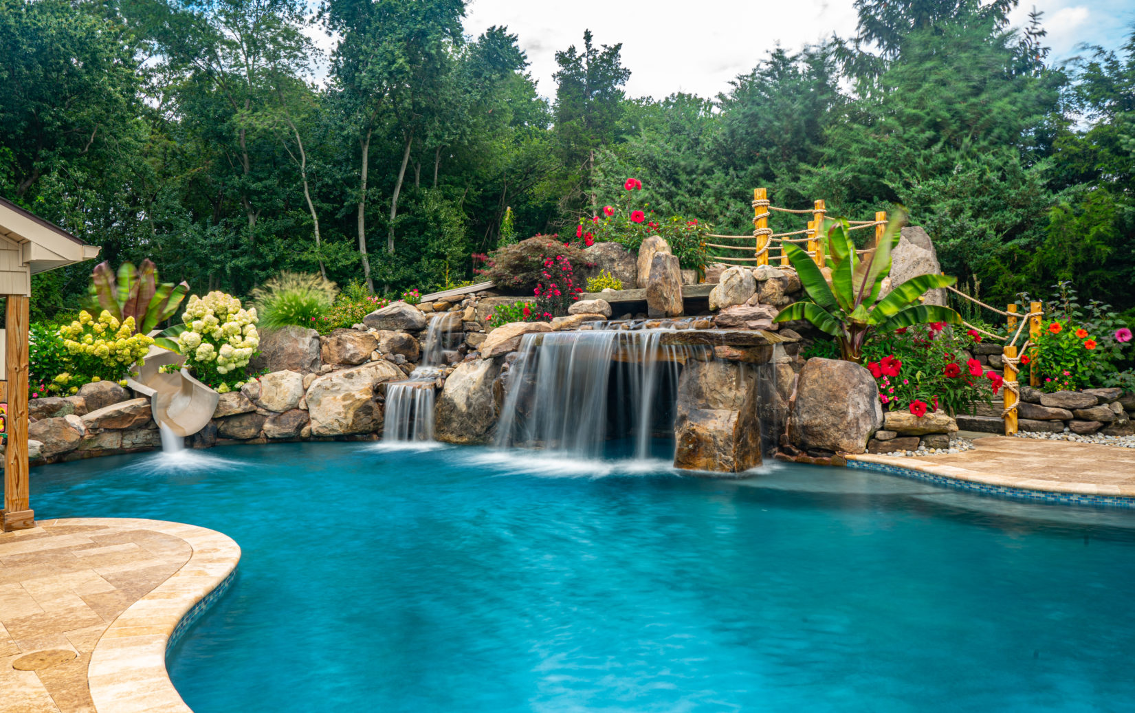 Aquatopia B - Williamstown, NJ - A swimming pool with a waterfall surrounded by lush greenery and colorful flowers