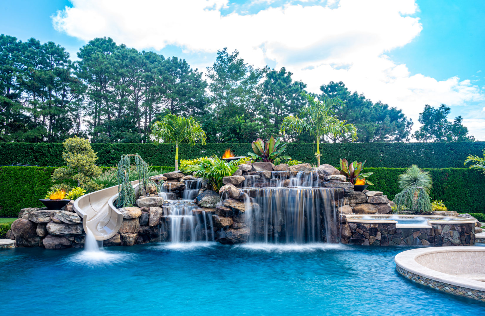 Aiello A - Monroe, NJ - A large swimming pool with a waterfall and a water slide surrounded by lush greenery