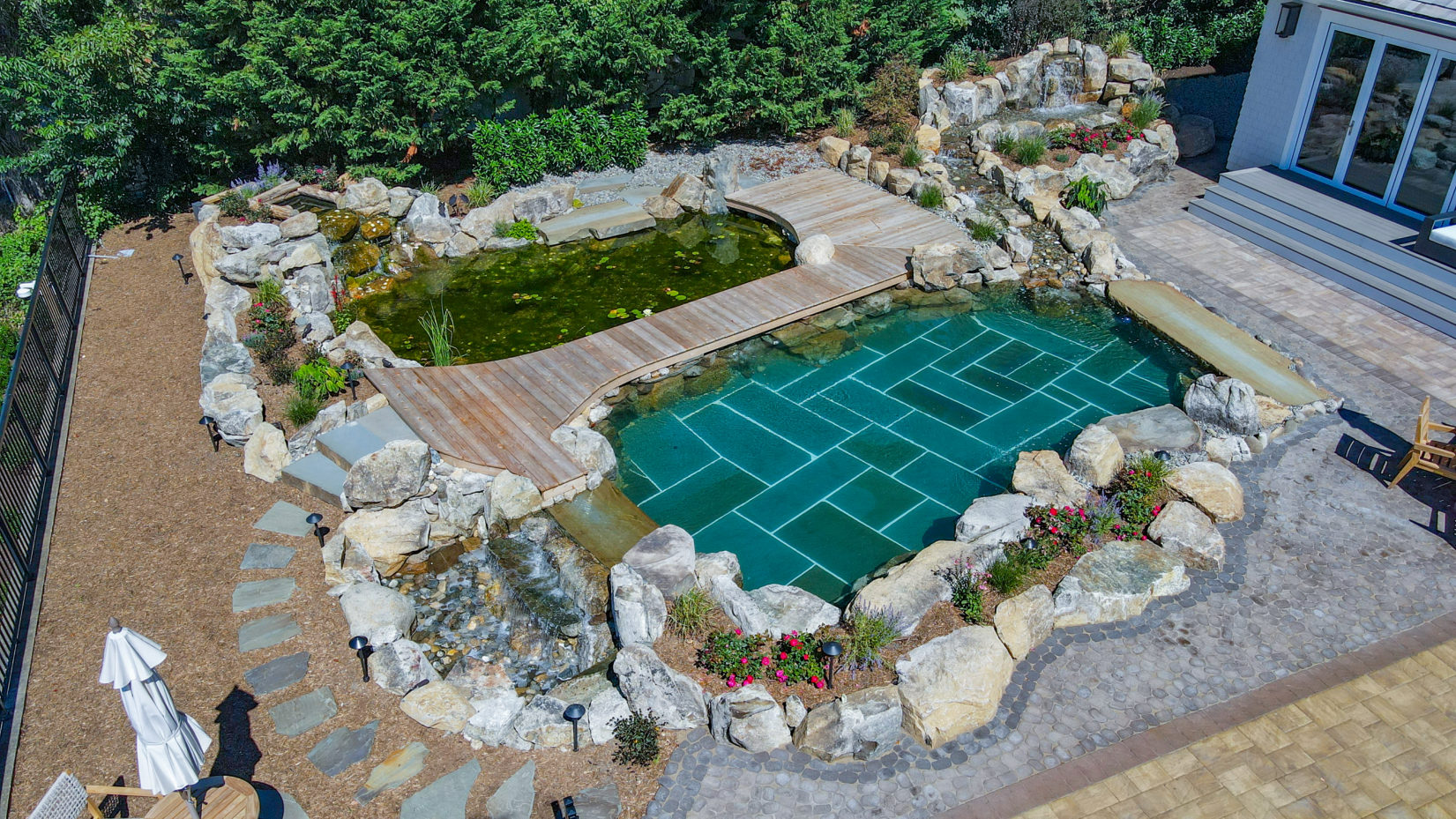 Day A - Manasquan, NJ - A bird's eye view of a backyard with a swimming pool surrounded by rocks and plants