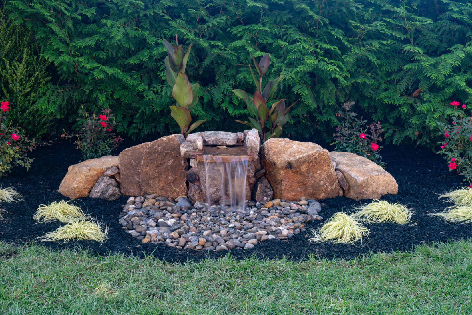 Genesis S -  - A small waterfall in the middle of a lush garden surrounded by plants and flowers
