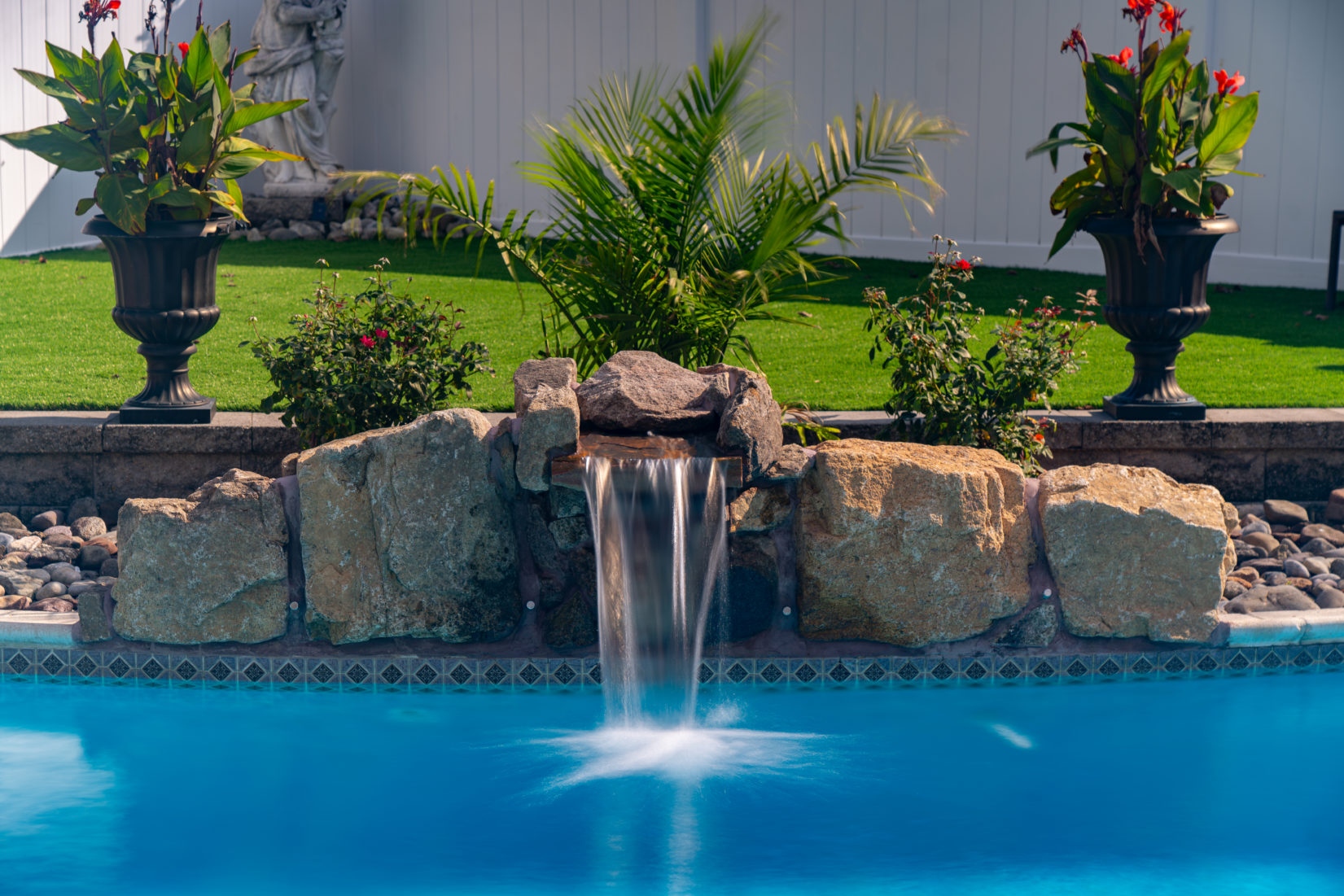 Saccamanno D - Cherry Hill, NJ - A swimming pool with a waterfall surrounded by lush greenery and potted plants