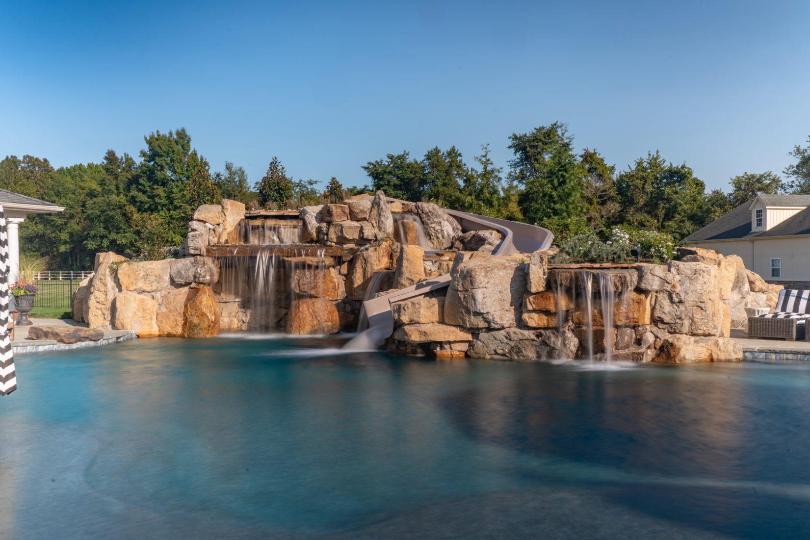 Radwell B - Medford, NJ - A large rock pool with a waterfall and a slide in a backyard setting