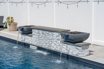 Dune L - Brigantine, NJ - A swimming pool with a water feature in the middle of it, surrounded by potted plants and string lights