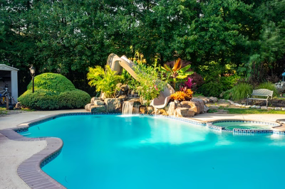 Alamere B - Colts Neck, NJ - A swimming pool with a water feature and a slide surrounded by lush greenery