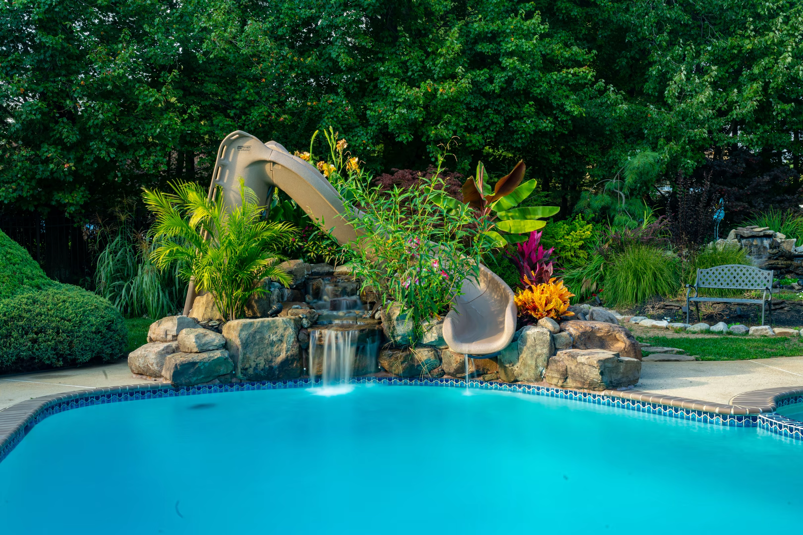 Two-tiered natural stone boulder waterfall cascading into a pool surrounded by lush tropical landscaping