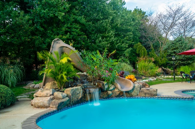 Alamere F - Colts Neck, NJ - A swimming pool with a water feature and a water slide surrounded by lush greenery