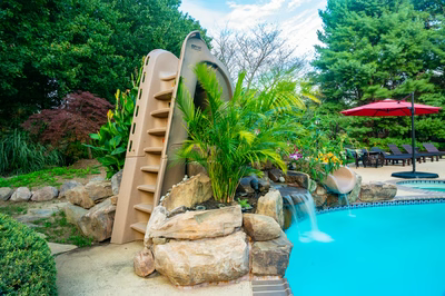 Alamere G - Colts Neck, NJ - A pool with a water feature and a water slide surrounded by lush greenery