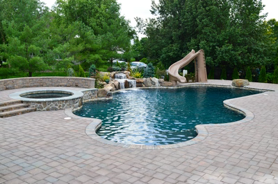 Alamosa D - Freehold, NJ - A swimming pool with a waterfall and a slide surrounded by lush greenery