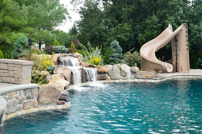 Alamosa E - Freehold, NJ - A swimming pool with a water feature and a slide in the background
