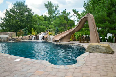 Alamosa H - Freehold, NJ - A swimming pool with a water feature and a slide in the background