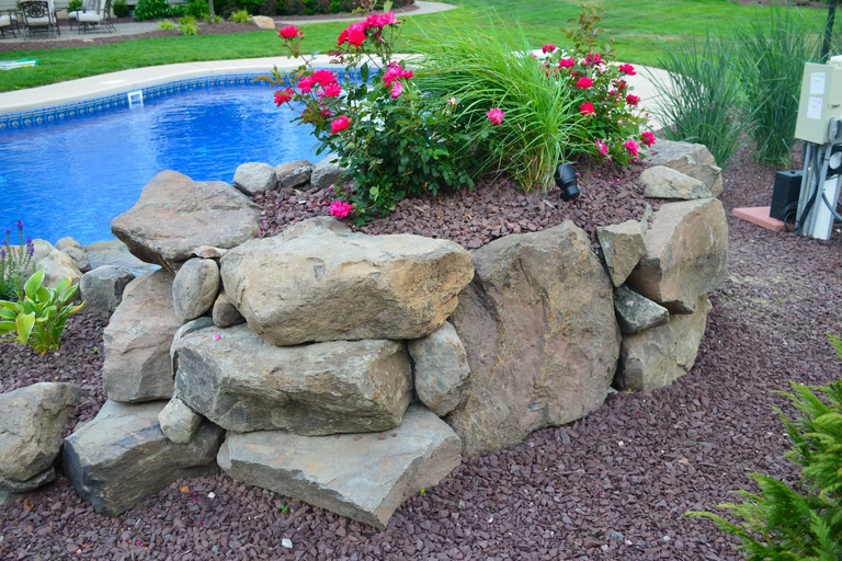 Natural stone boulder waterfall cascading into a blue pool with vibrant floral landscaping