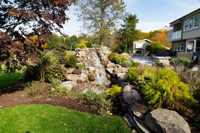 Alpine C - Moorestown, NJ - A backyard with a waterfall surrounded by rocks and greenery