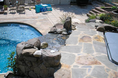 Angel J - Voorhees, NJ - A backyard with a swimming pool and a stone waterfall feature