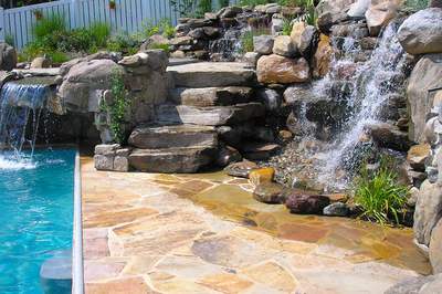 Angel K - Voorhees, NJ - A pool with a waterfall and a stone patio next to it