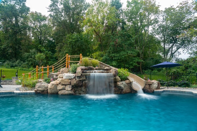 Antelope A - Ringoes, NJ - A swimming pool with a waterfall and a slide surrounded by lush greenery