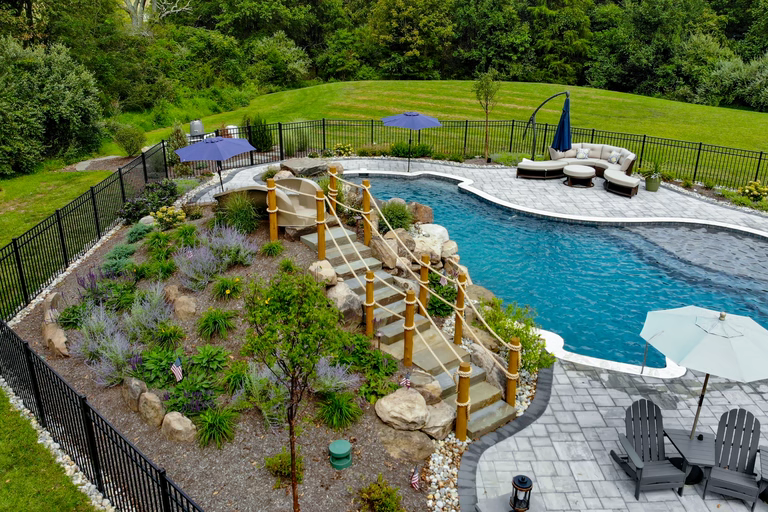 Natural stone boulder waterfall cascading into a freeform pool with lush garden plants