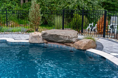 Antelope H - Ringoes, NJ - A swimming pool with a rock feature and a black fence surrounding it