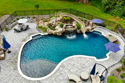 Antelope I - Ringoes, NJ - A backyard with a swimming pool, a waterfall, and a play area surrounded by lush greenery