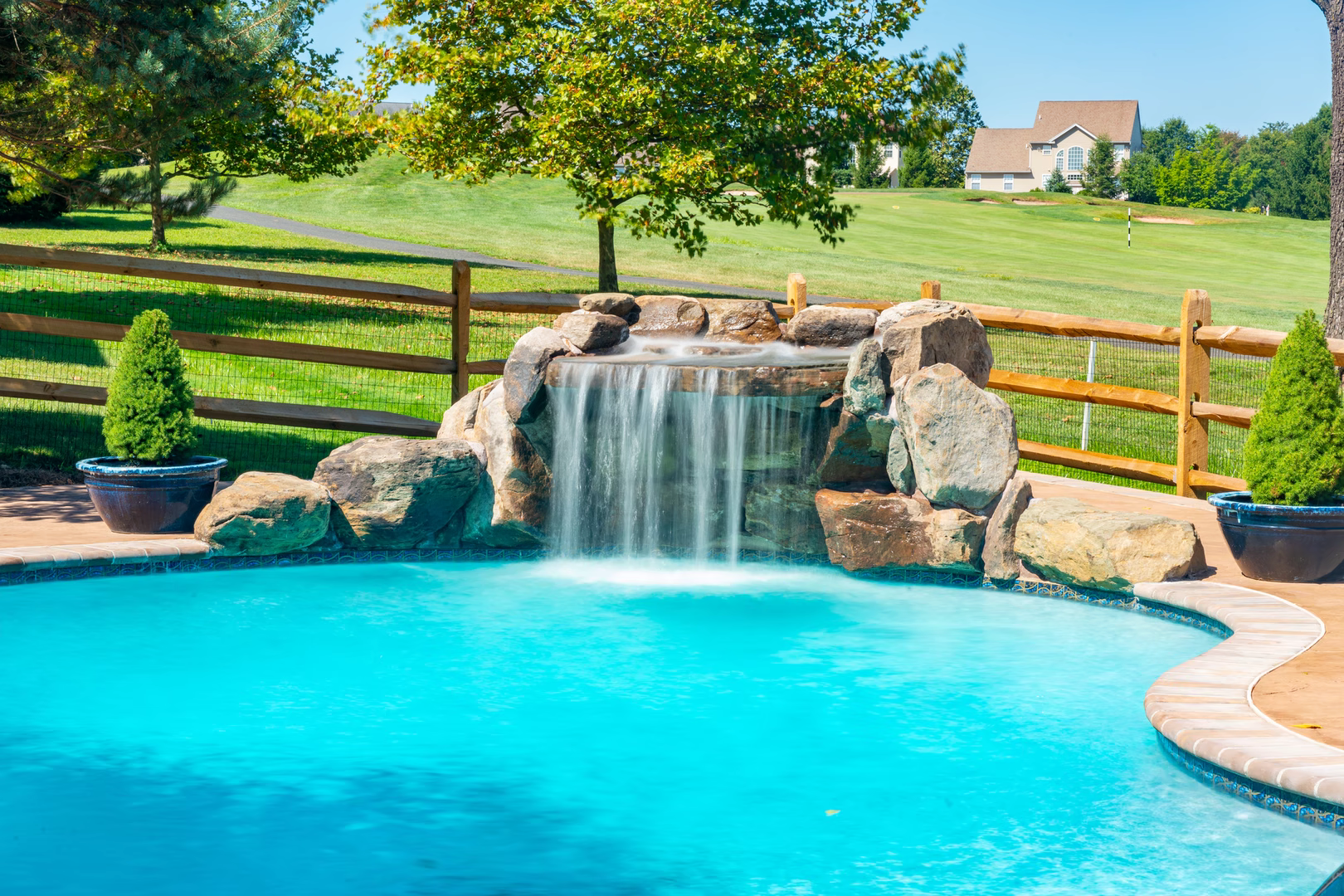 Single-tier natural stone boulder waterfall with sheet flow cascading into a pool near plants