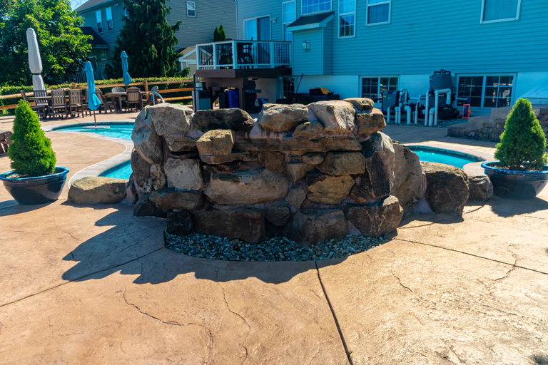 Natural stone boulder waterfall cascading into a pool beside potted evergreen shrubs