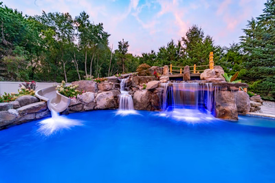 Aquatopia A - Williamstown, NJ - A beautiful garden with a waterfall and a wooden bridge over a pool surrounded by lush greenery and colorful flowers