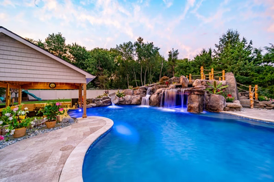 Aquatopia D - Williamstown, NJ - A swimming pool with a waterfall surrounded by lush greenery and colorful flowers