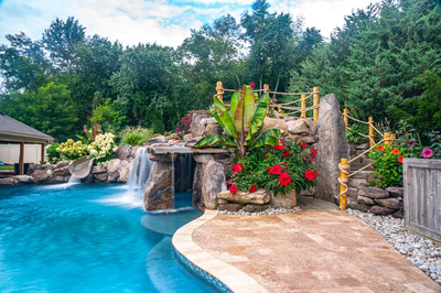 Aquatopia H - Williamstown, NJ - A beautiful backyard with a pool and a waterfall surrounded by lush greenery and colorful flowers