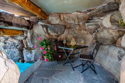 Aquatopia M - Williamstown, NJ - A small table and two chairs set up in a stone cave-like setting with pink flowers and a bottle of wine