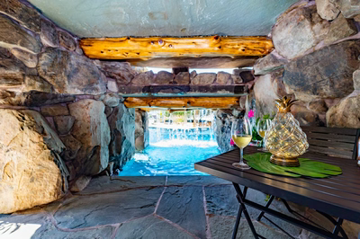 Aquatopia N - Williamstown, NJ - A table with two glasses of white wine and a pineapple vase on it, set against a stone wall with a waterfall in the background