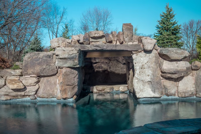 Armstrong C - Moorestown, NJ - A large stone structure with a pool in front of it, surrounded by trees and a clear blue sky