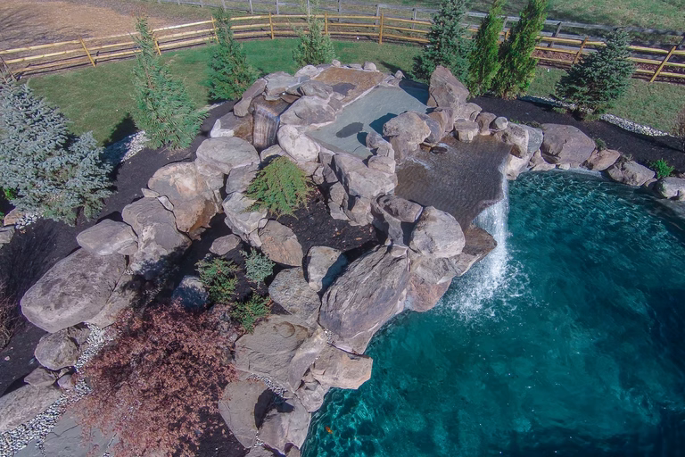 Natural stone boulder waterfall cascading into a pool with lush evergreen landscaping