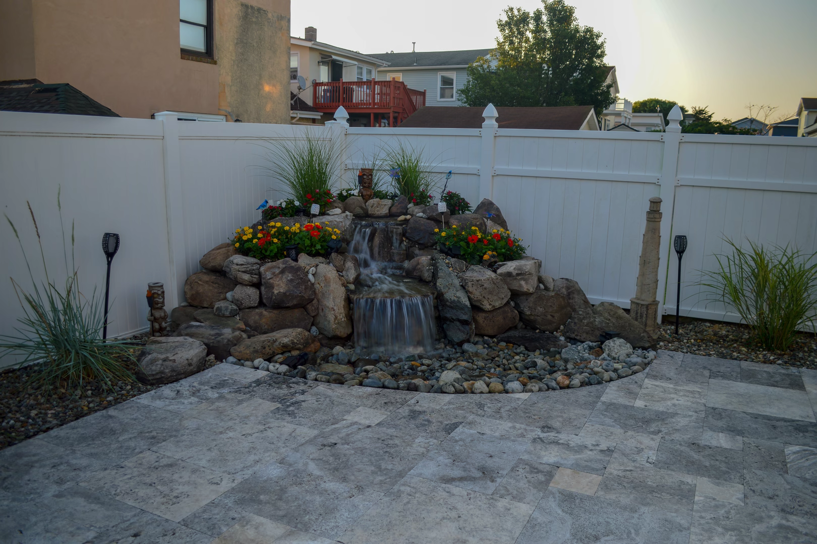 Two-tiered natural stone boulder waterfall cascading into a basin surrounded by lush garden plants