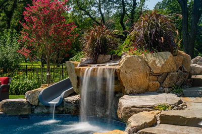 Augrabies E - West Deptford, NJ - A pool with a waterfall and a slide surrounded by lush greenery