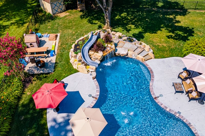 Augrabies K - West Deptford, NJ - A backyard with a swimming pool and a water feature surrounded by lush greenery and colorful flowers