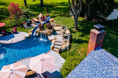 Augrabies L - West Deptford, NJ - A backyard with a swimming pool and a water feature, surrounded by lush green grass and trees