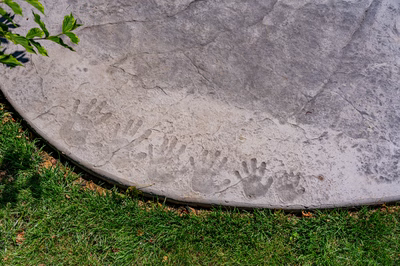Augrabies N - West Deptford, NJ - A close-up of a concrete surface with handprints on it, surrounded by green grass
