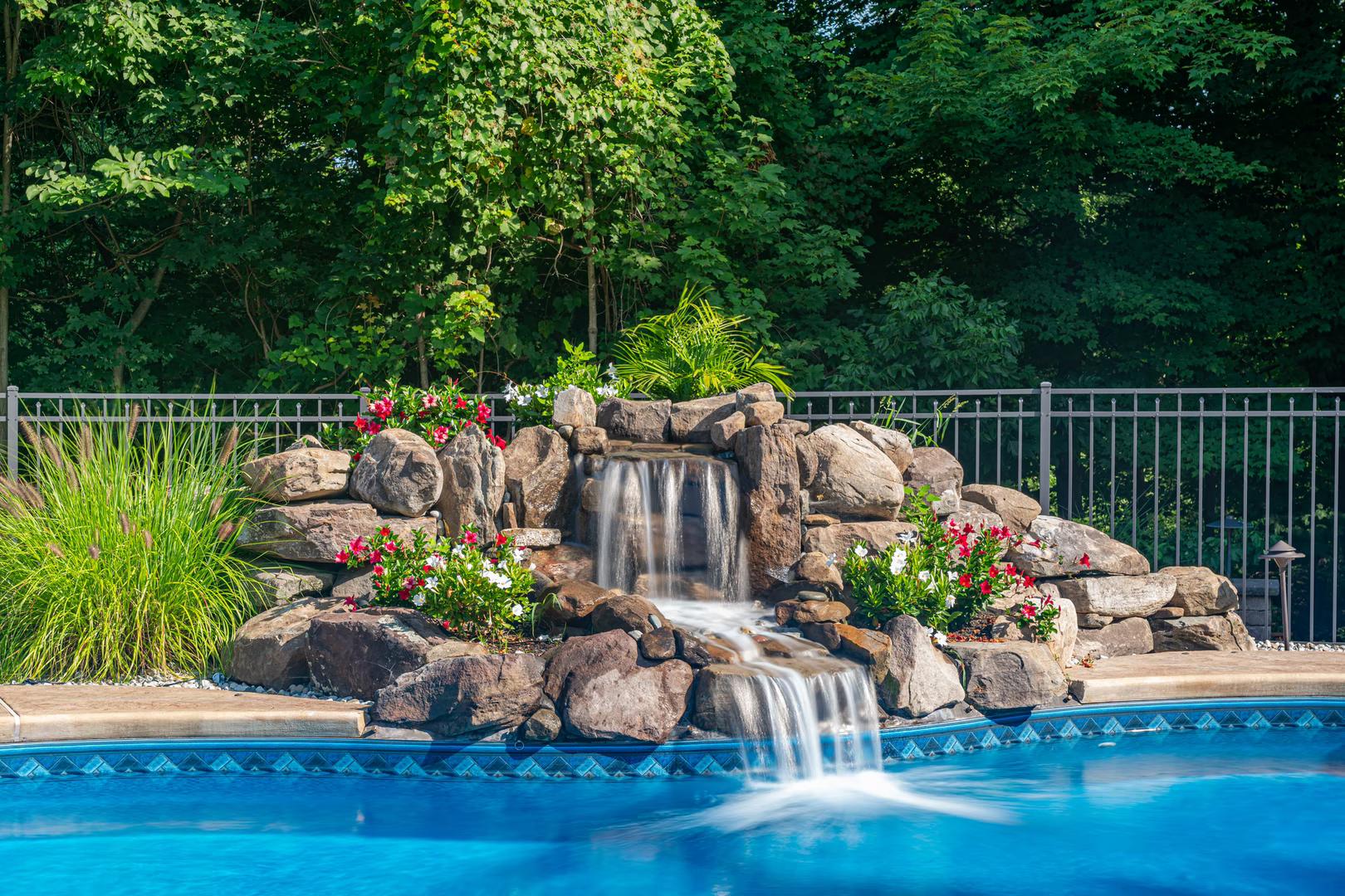 Two-tiered natural stone boulder waterfall cascading into a pool with lush floral landscaping