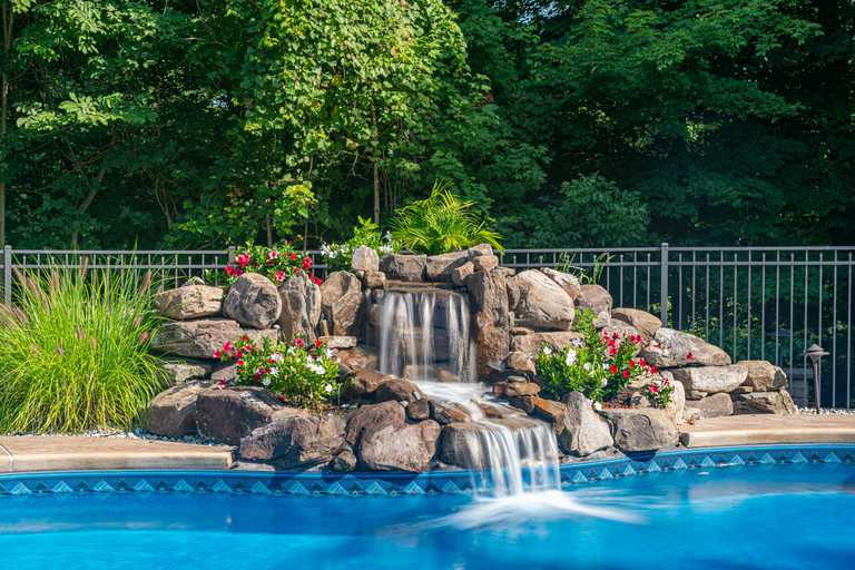 Natural stone boulder waterfall cascading into a pool with lush floral landscaping