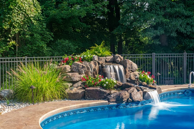 Azure C - Hillsborough, NJ - A swimming pool with a waterfall surrounded by lush greenery and flowers