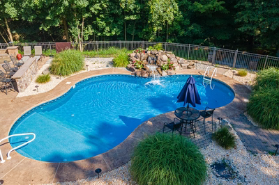 Azure H - Hillsborough, NJ - A backyard with a swimming pool surrounded by greenery and a waterfall