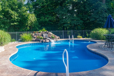 Azure I - Hillsborough, NJ - A blue swimming pool surrounded by lush greenery and a waterfall.