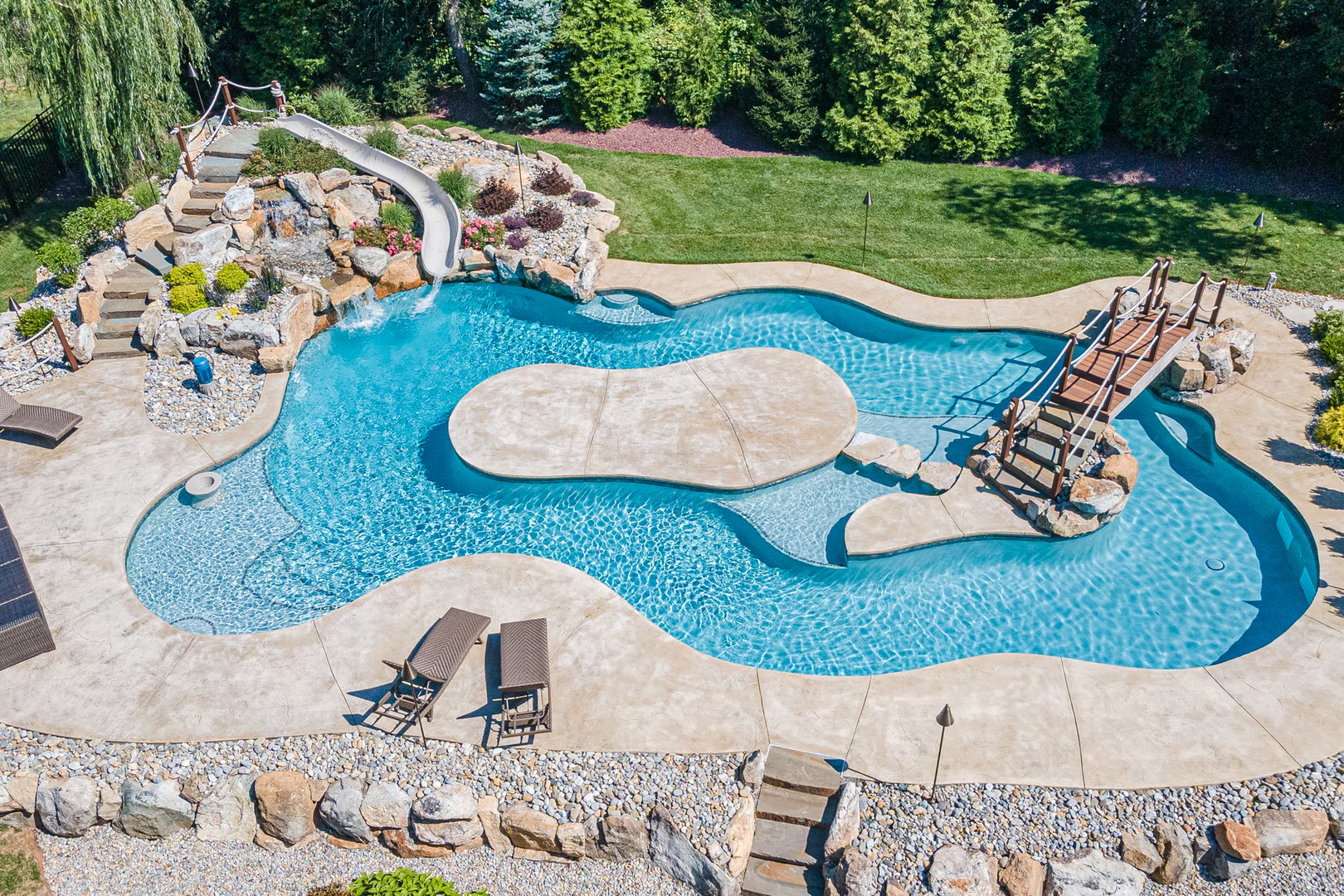 Multi-tiered natural stone boulder waterfall cascading into a freeform pool with lush green landscaping