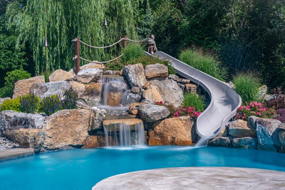 Bagley C - Williamstown, NJ - A swimming pool with a waterfall and a slide surrounded by lush greenery