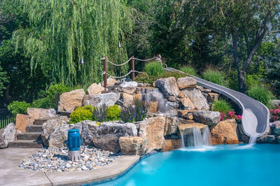Bagley D - Williamstown, NJ - A swimming pool with a waterfall and a water slide surrounded by lush greenery
