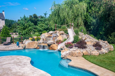 Bagley E - Williamstown, NJ - A swimming pool with a waterfall and a water slide surrounded by lush greenery