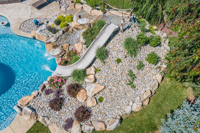 Bagley I - Williamstown, NJ - A backyard with a swimming pool and a water slide surrounded by rocks and plants