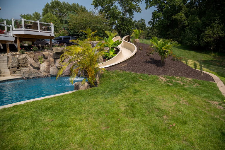 Natural stone boulder waterfall cascading into a pool surrounded by lush tropical plants