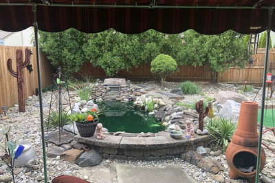 Basin A - Wenonah, NJ - A backyard with a small pond surrounded by rocks and plants under a striped awning