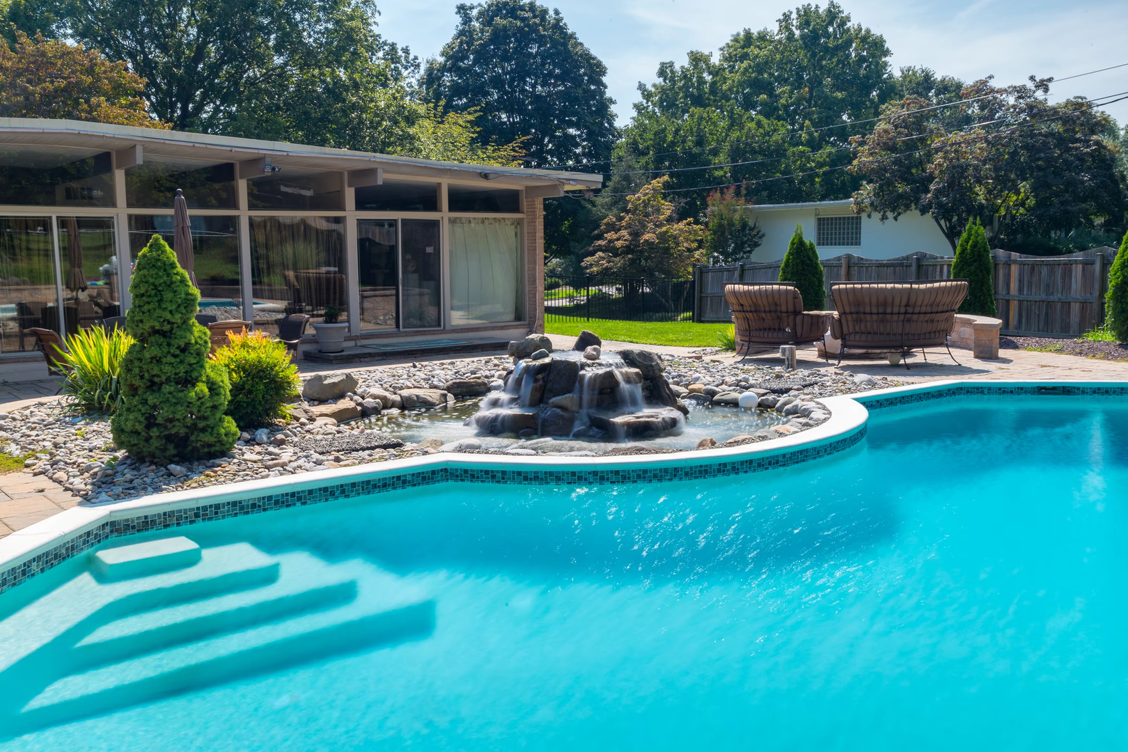 Cascading multi-tiered natural stone waterfall flowing into a clear pool beside lush garden plants